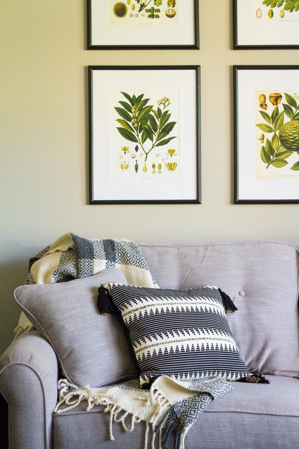 Botanical prints arranged in a grid above a gray couch; black and white accent pillows