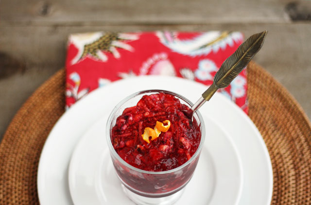 a wooden background with a single red and white place setting, featuring a dish of red cranberry jello with a slice of orange peel on top