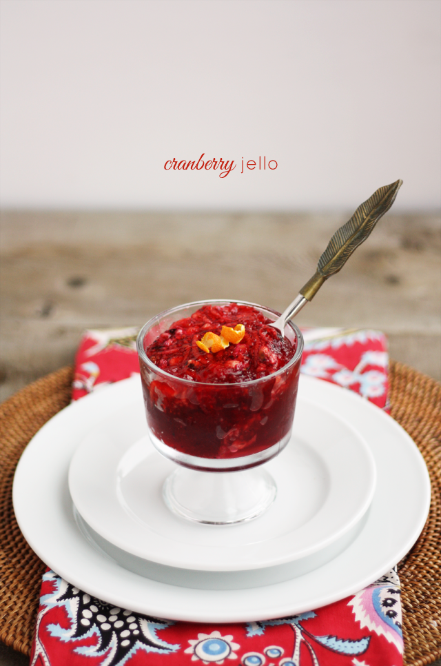 a wooden background with a single red and white place setting, featuring a dish of red cranberry jello with a slice of orange peel on top