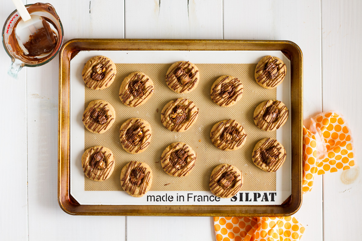 A classic peanut butter cookie with a twist! This delicious Candy Bar Thumbprint Cookies combine your favorite peanut butter cookie with chopped up candy bars and a drizzle of melted milk chocolate!