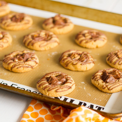 A classic peanut butter cookie with a twist! This delicious Candy Bar Thumbprint Cookies combine your favorite peanut butter cookie with chopped up candy bars and a drizzle of melted milk chocolate!
